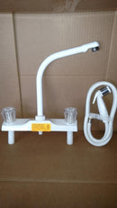 White high rise kitchen faucet with sprayer and two handles, displayed against a cardboard background.